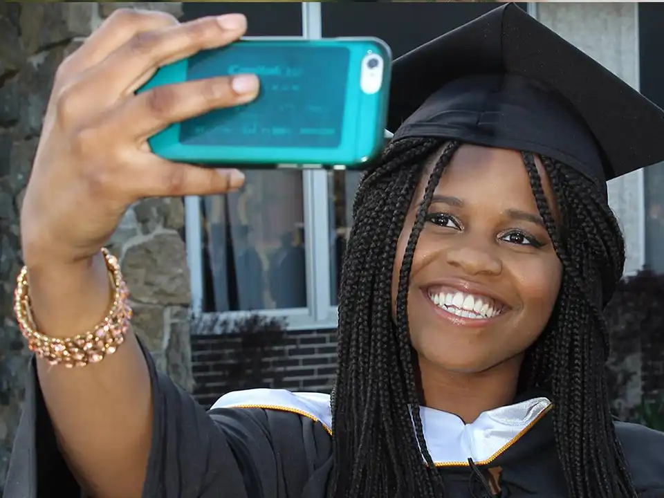 Smiling student in cap and gown taking selfie