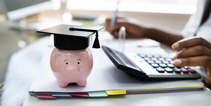 Piggy bank with grad cap next to person using calculator