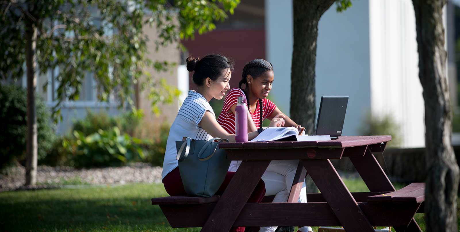 Students sitting in picnic table working together outside 